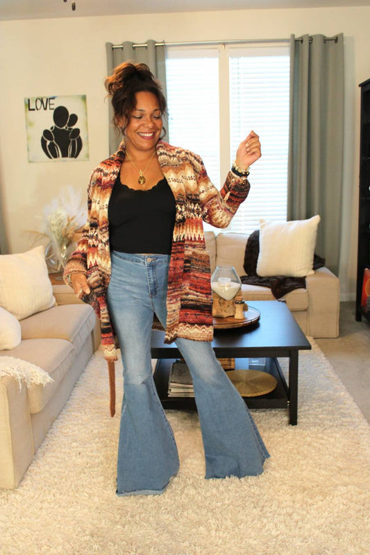 Model wearing a red, orange, brown, and white striped cardigan, black tank top, and blue wide flare jeans.