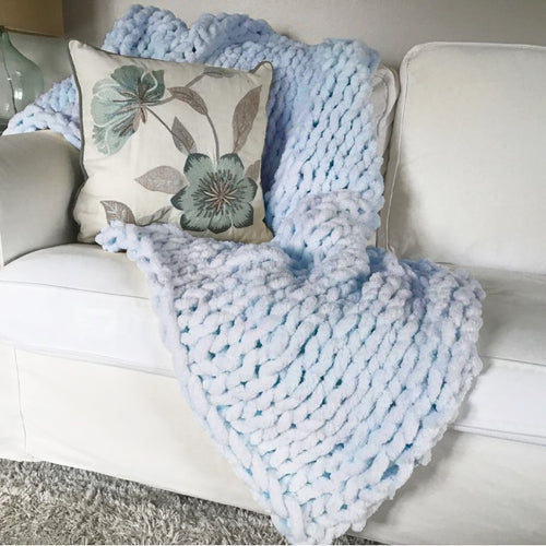 Sky blue chunky and fuzzy hand knit blanket draped on couch.