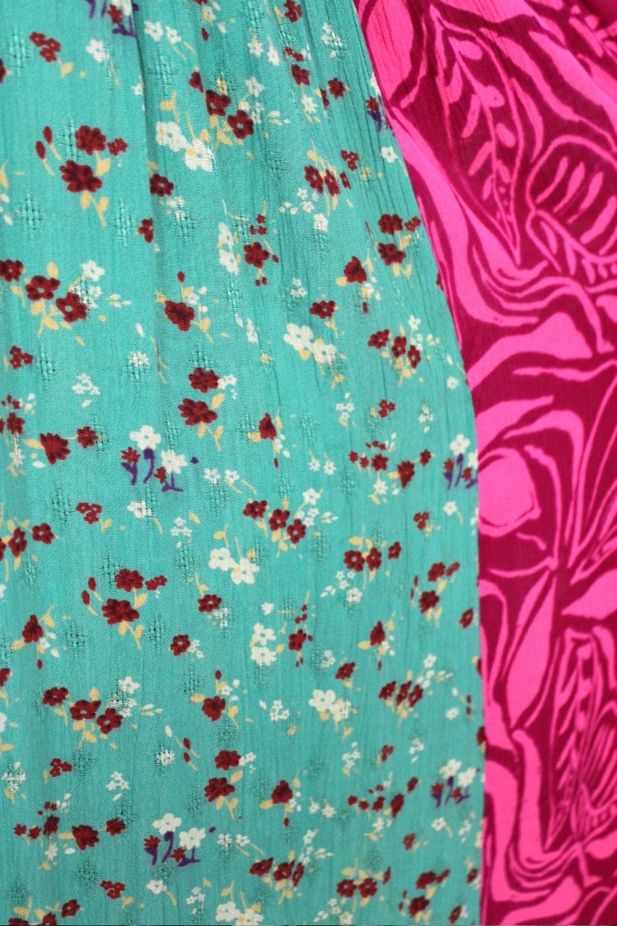 Close-up of teal fabric with floral pattern and pink fabric with abstract design.