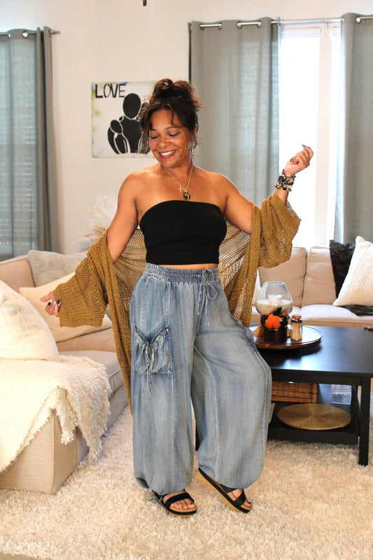 Model wearing a black tube top, bronze toned lace knit cardigan, light blue flowy denim pants.