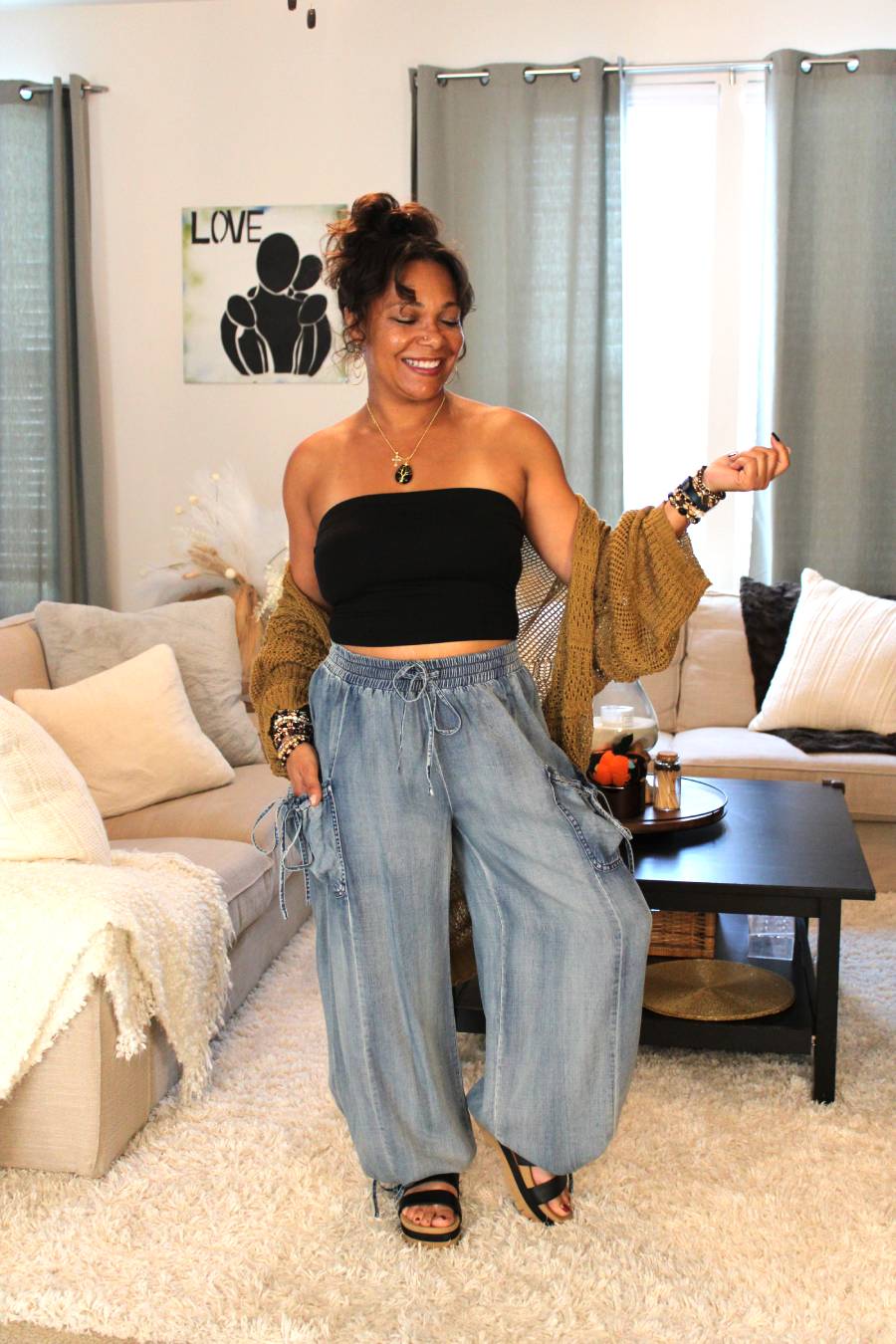 Model wearing a black tube top, bronze toned lace knit cardigan, light blue flowy denim pants.