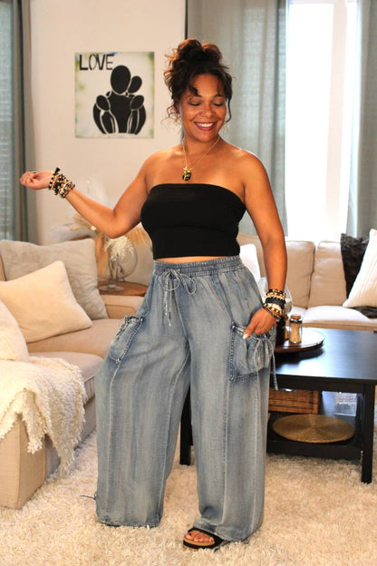Model posing in black tube top and light blue flowy denim pants.