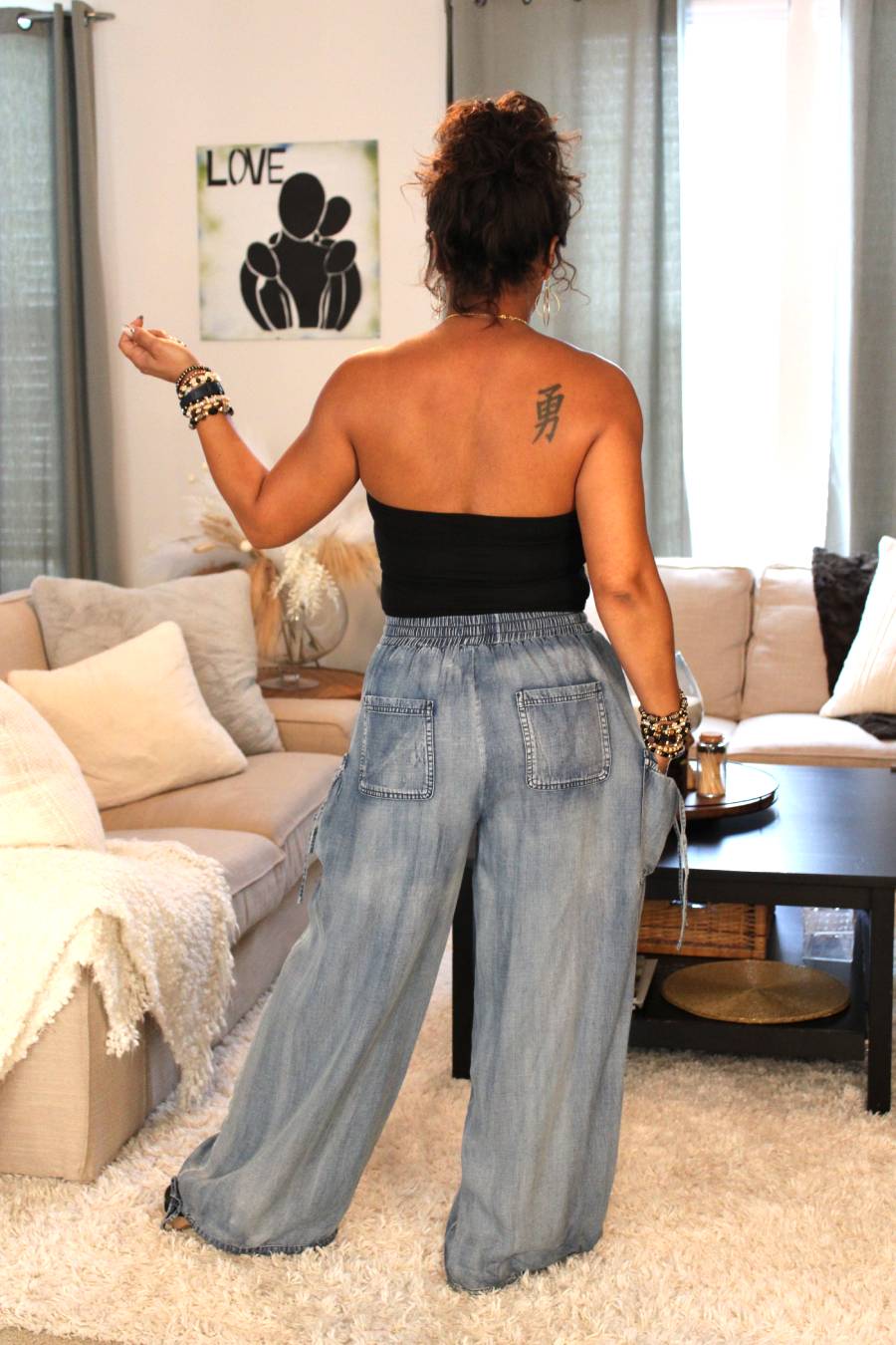 Model showcasing the back of a black tube top and light blue flowy denim pant outfit.