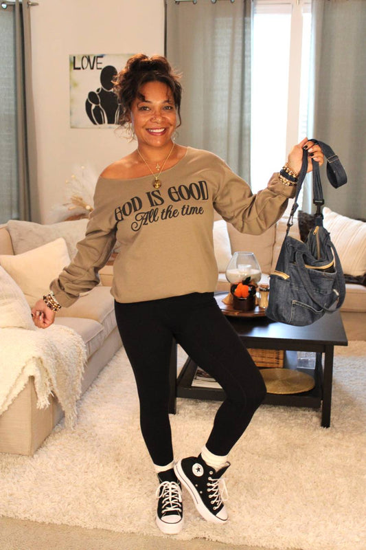 Model holding a recycled denim handbag, wearing a 'God is Good All the Time' brown sweatshirt.