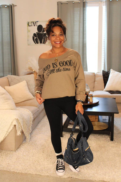 Model holding a blue recycled denim handbag, wearing a 'God is Good' brown sweater.