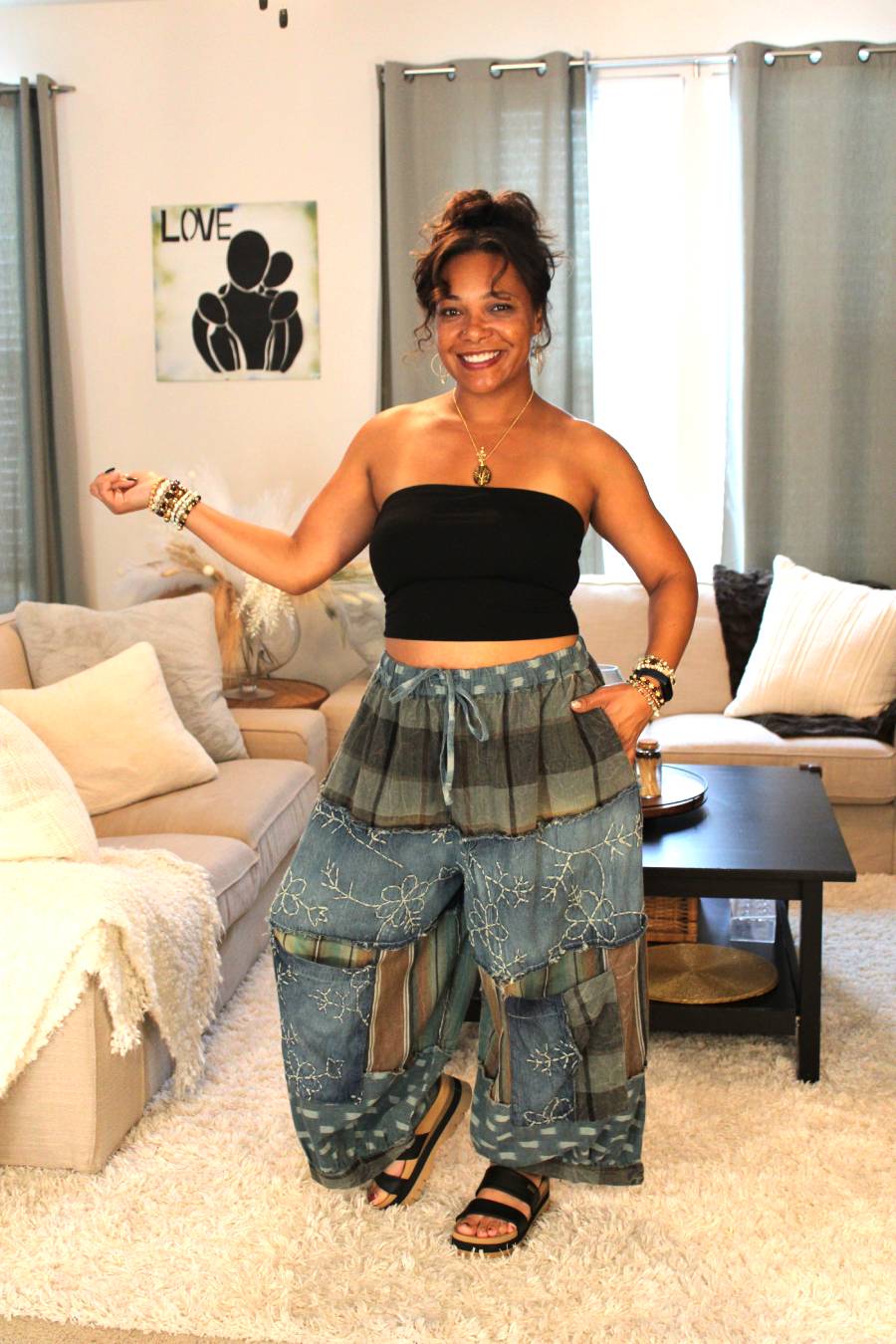 Woman wearing a black tube top and blue patchwork pants posing towards the side.