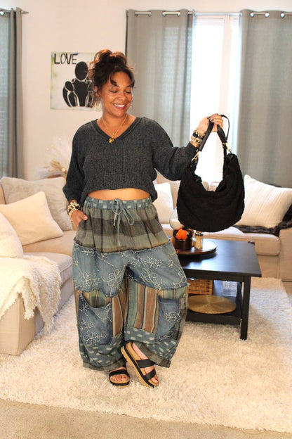 Model wearing a dark gray sweater and blue patterned pants. Holding black fuzzy handbag.