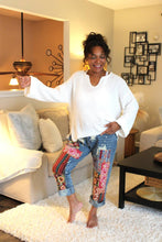 Load image into Gallery viewer, Woman in a living room wearing a white sweater and colorful pants.
