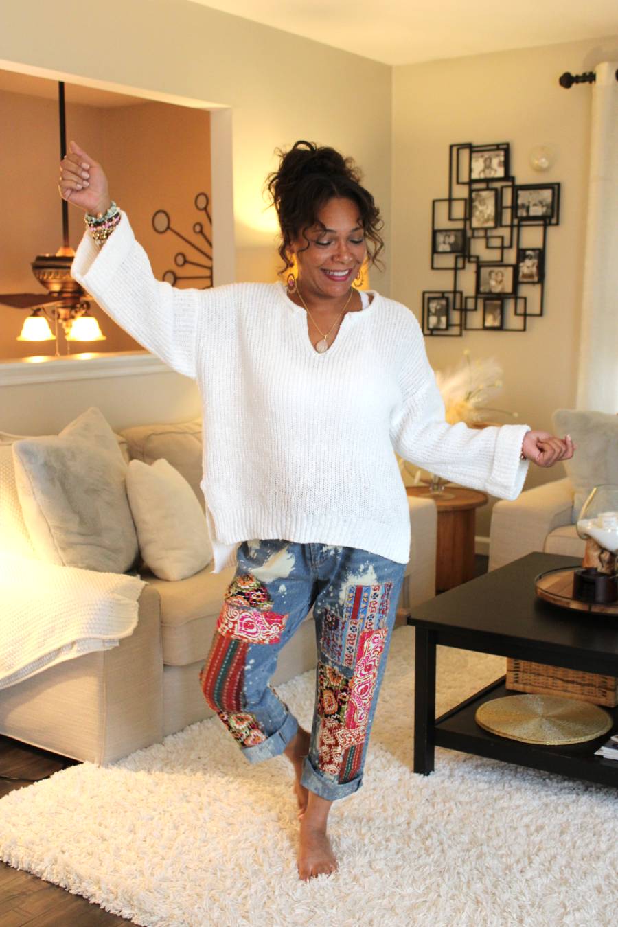 Woman in a white, soft sweater and colorful pants standing in a living room.