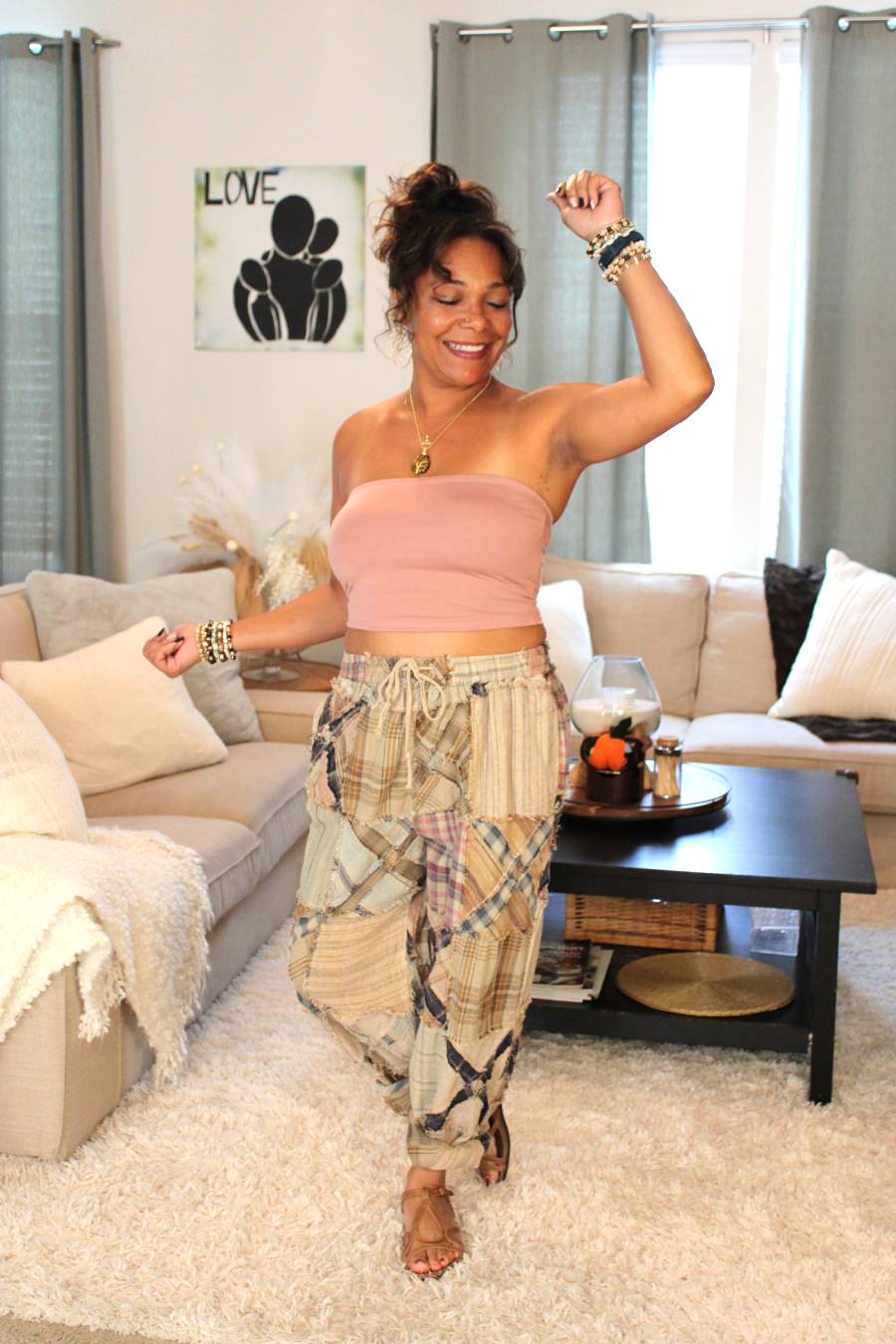 Model posing in a carefree way wearing a pink bamboo tube top and plaid pants featuring an x pattern similar to railroad crossings.