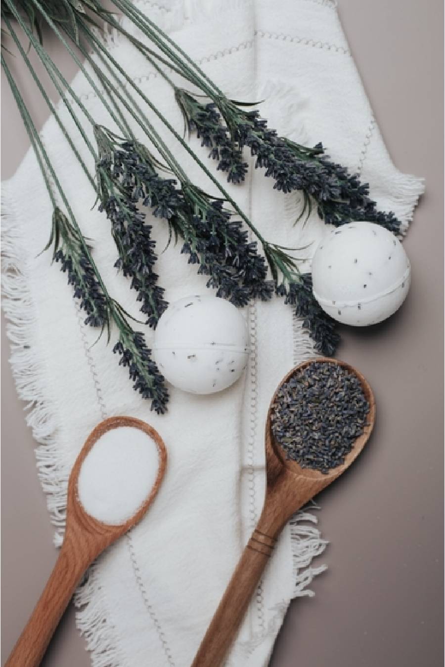 White bath bombs, lavender flowers, and wooden spoons with lavender on a white towel.