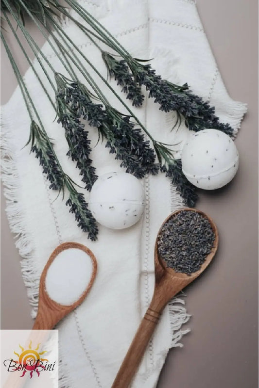 White bath bombs, lavender flowers, and wooden spoons with lavender on a white towel.
