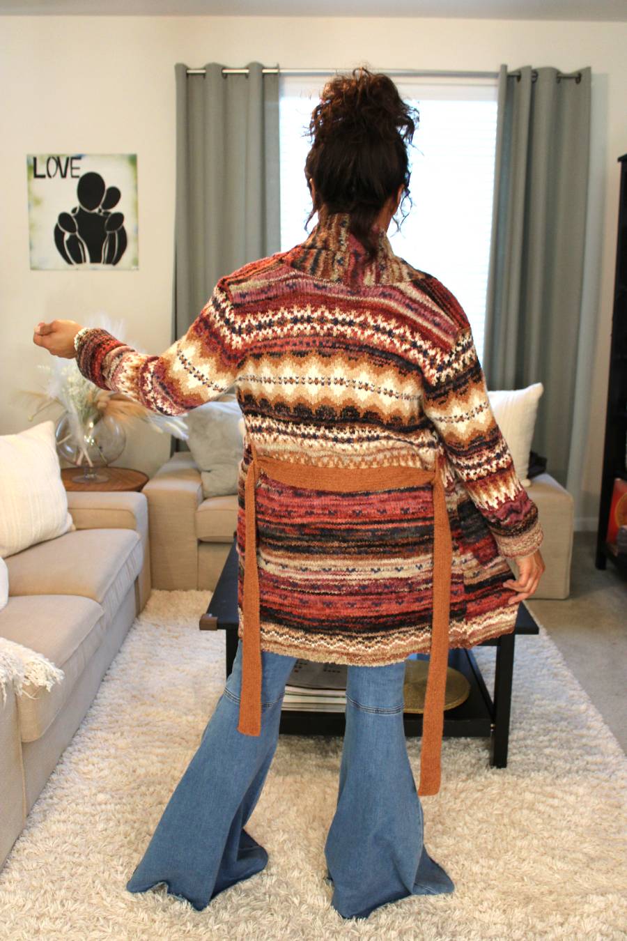 Model showcasing the backside of the red, orange, brown, and white striped cardigan. She's also wearing blue wide flare jeans.