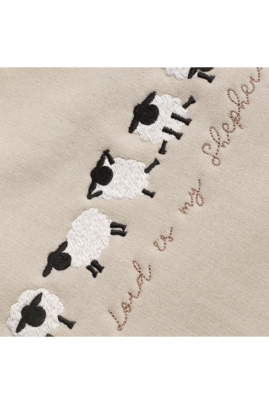 Close-up of the embroidered sheep on the beige sweatshirt doing cute yoga poses.